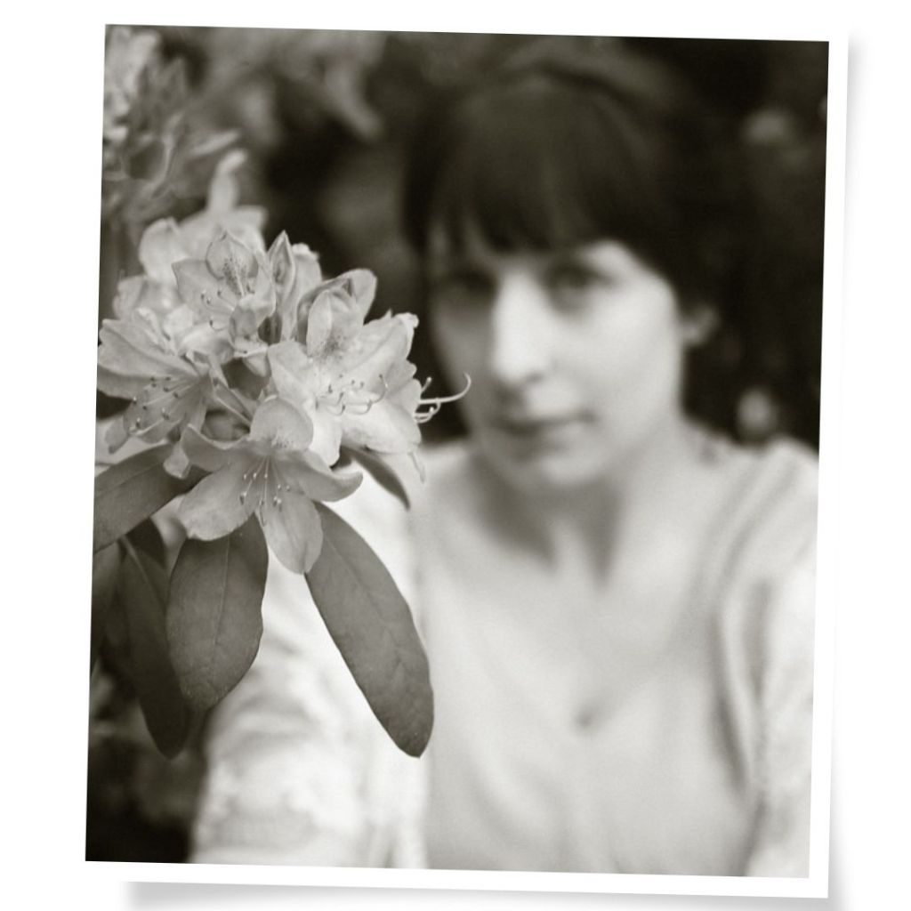 Portrait einer Frau zwischen blühendem Rhododendron, Ateliergarten in Limbach-Oberfrohna, bei Chemnitz, Sommerlicht.