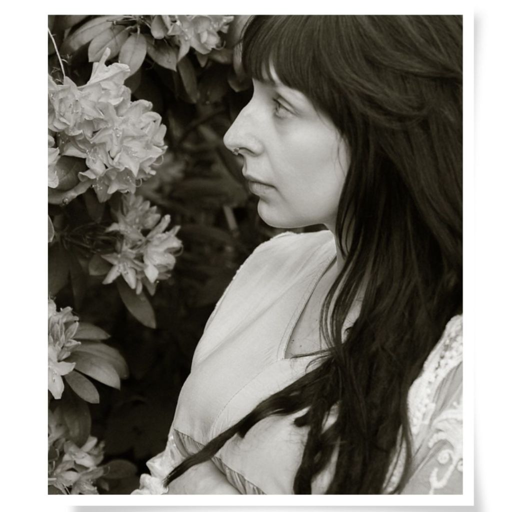 Portrait einer Frau zwischen blühendem Rhododendron, Ateliergarten in Limbach-Oberfrohna, bei Chemnitz, Sommerlicht.